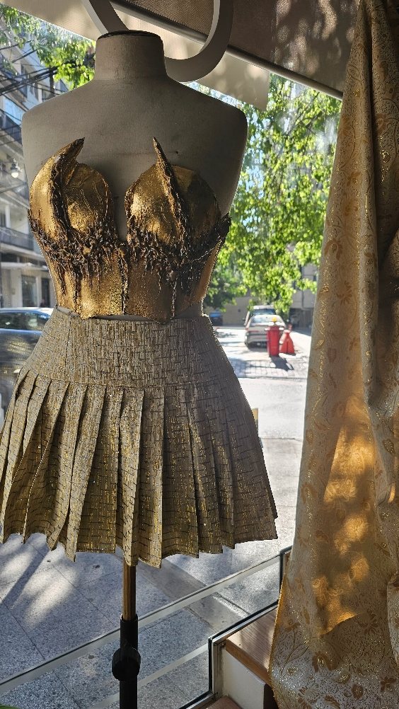 Gold sculpted bustier and pleated metallic skirt displayed in the Aura atelier window