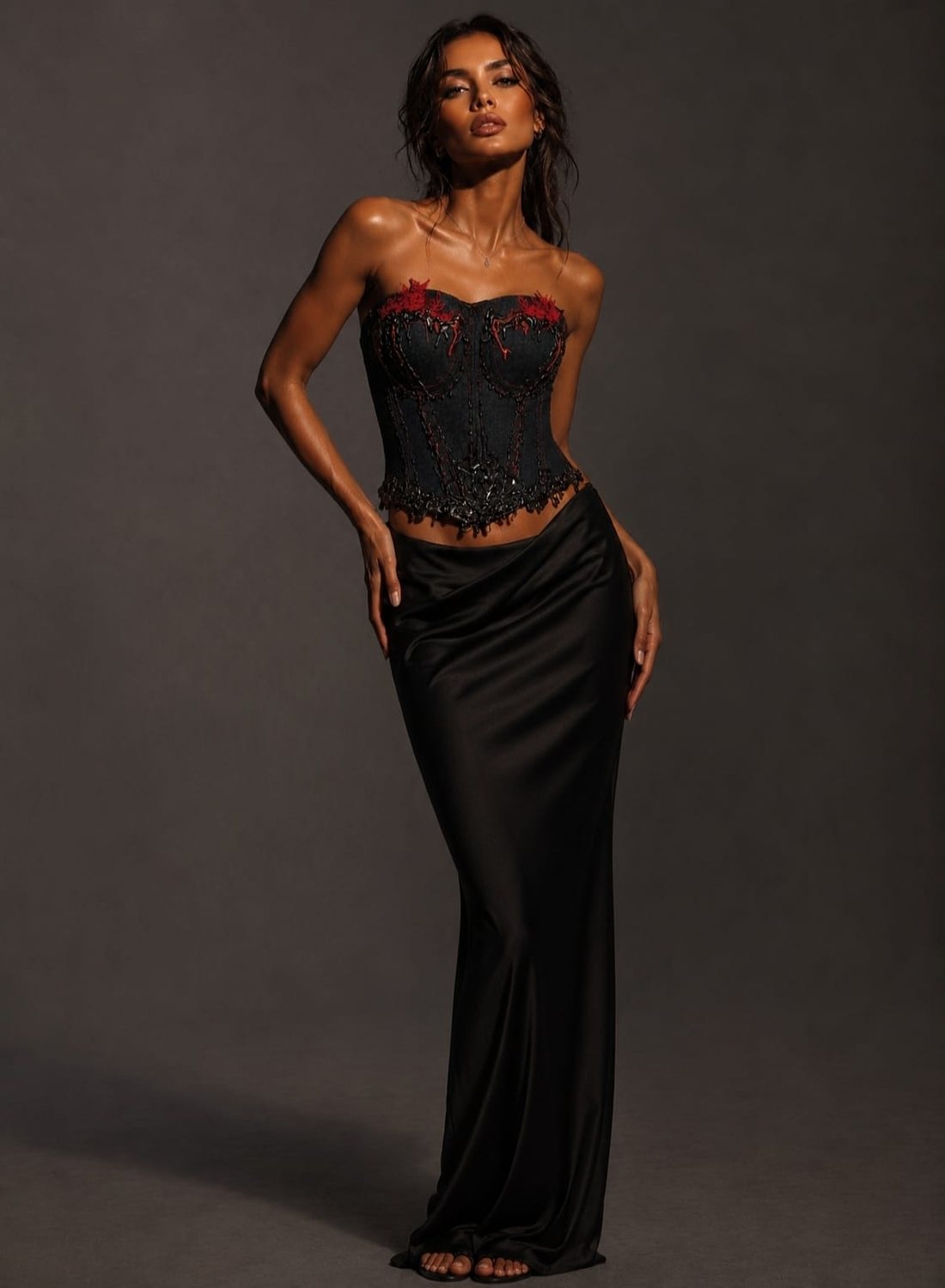Hand-embellished denim corset with red and black detailing, worn with a black satin maxi skirt